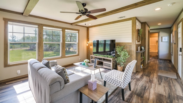 A spacious living room with a gray sofa, a wooden coffee table, and a television. There are large windows providing natural light and a view of the outdoors. - Pet-friendly Hill Country Hideaway w/ Deck (D'Hanis)