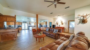 A spacious living room with a leather sofa, wooden flooring, and a ceiling fan. - Texas Nature Escape: Lake & Game Room Access (D'Hanis)