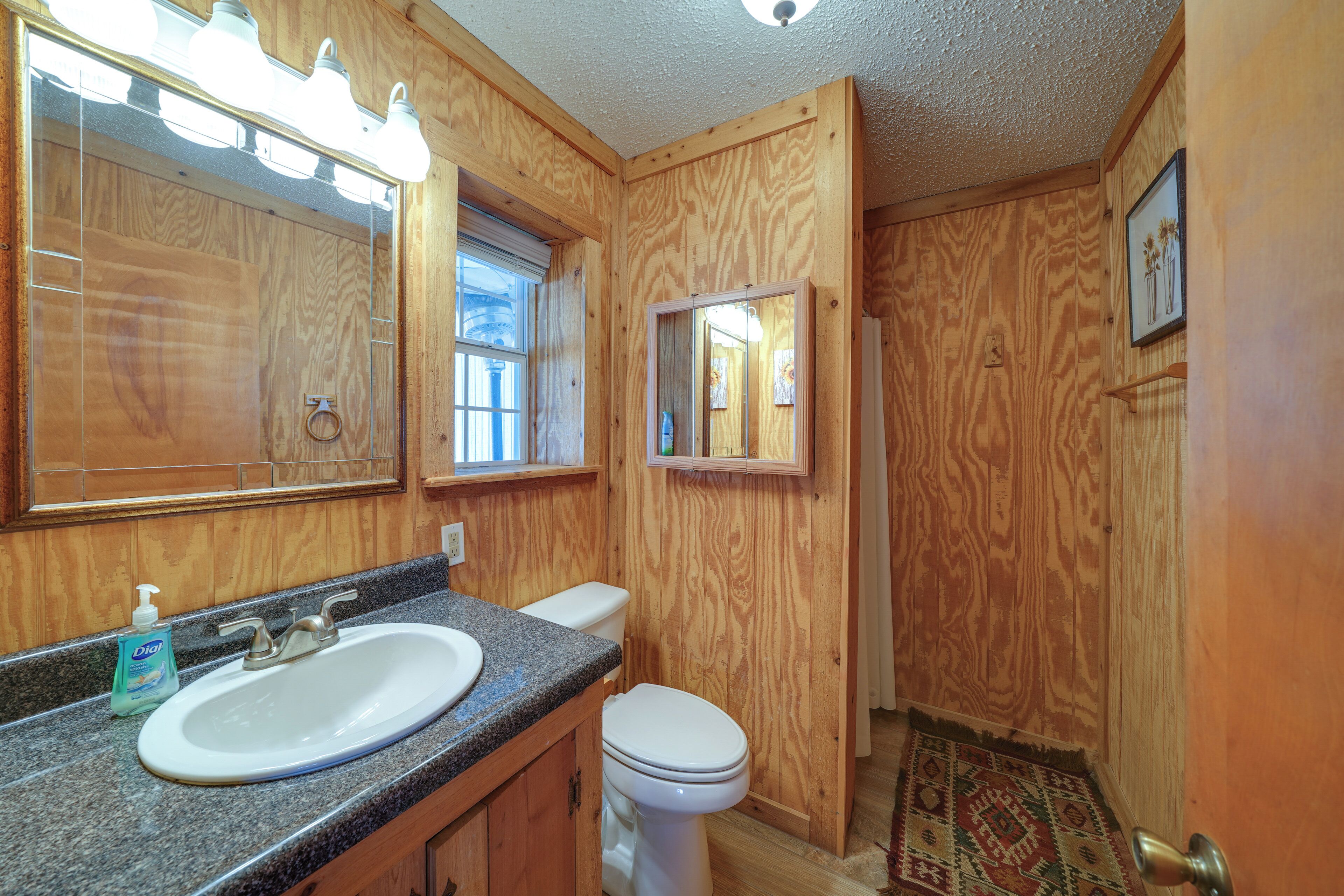 A wooden-paneled bathroom with a sink, toilet, and mirror.