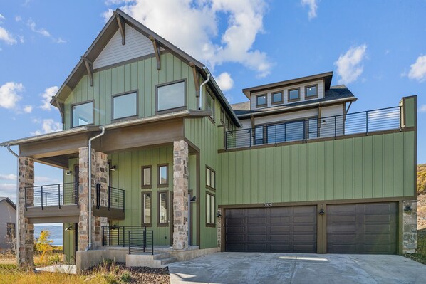 Une maison à deux étages, avec des fondations en pierre, un revêtement extérieur vert et un grand garage.