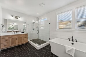 Une salle de bain moderne dotée d’une douche à parois de verre, d’une grande baignoire et d’un meuble-lavabo avec un miroir et un évier.