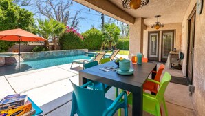 Un patio al aire libre con piscina, sillas y una mesa con platos y vasos.
