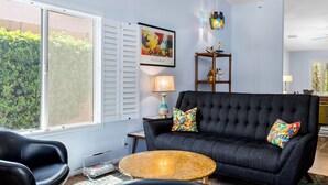 Una sala de estar con un sofá oscuro, una mesa redonda y una ventana con contraventanas.