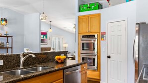 Una cocina con encimeras de granito, electrodomésticos de acero inoxidable, armarios de madera y un estante verde en la pared.