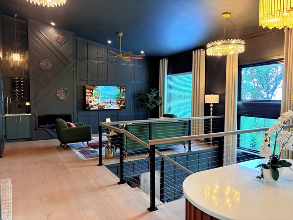 A modern living room with a television, seating, a staircase, and a view of the outdoors.
