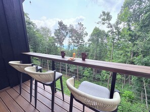 Un balcon avec deux chaises et une table, donnant sur une zone boisée.