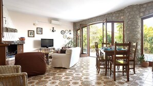 A living room with a fireplace, a television, a dining area with a table and chairs, and a patterned floor. - Solemar Sicilia - Villa Corallo (Bagheria)