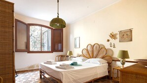A bedroom with a bed, wicker furniture, a window with curtains, and patterned floor tiles. - Solemar Sicilia - Villa Corallo (Bagheria)