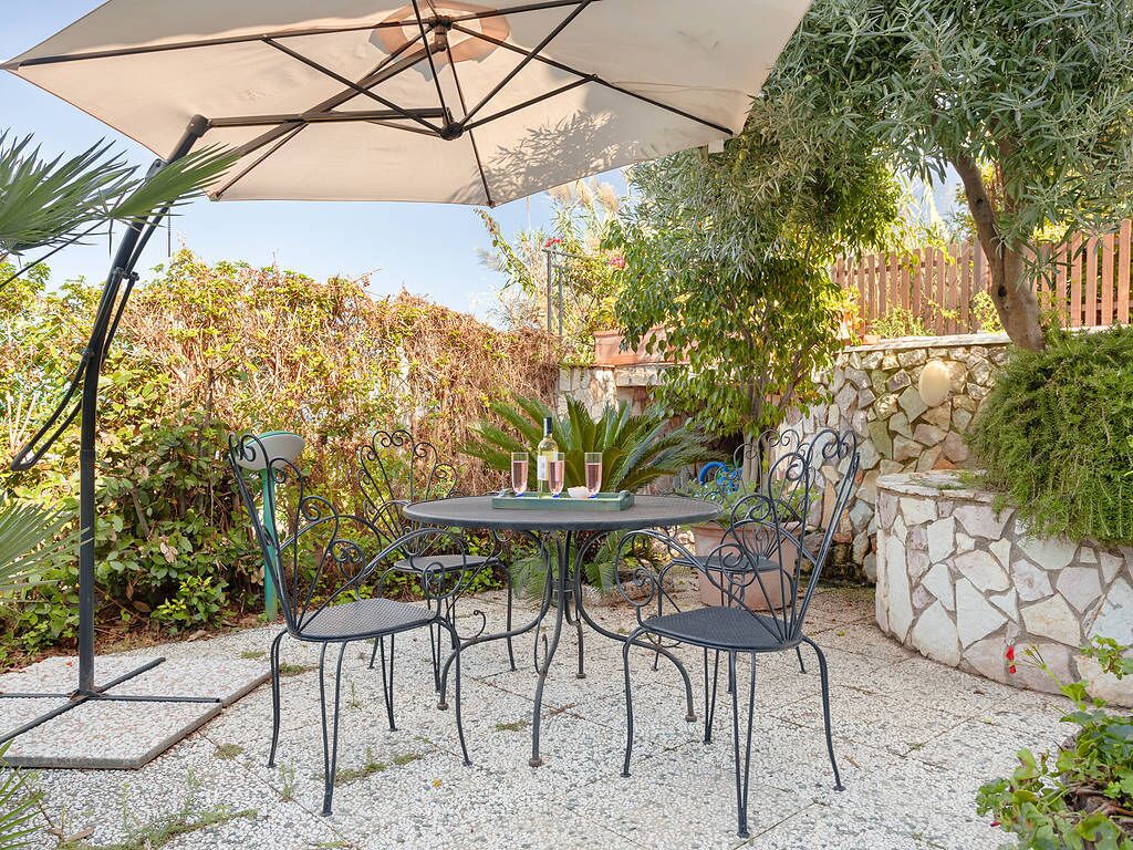 Een terras met een ronde tafel, vier stoelen, een parasol en een stenen muur.