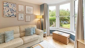 Una sala de estar acogedora con un sofá color crema, un aparador de madera y vistas a un jardín a través de amplios ventanales.