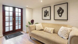 A living room with a beige sofa, two decorative pillows, a framed abstract artwork, and a wooden door with frosted glass panels. - Host & Stay | Yule House (Alnwick)