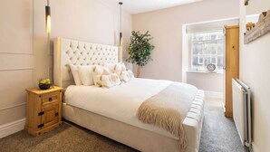 A bedroom with a large bed, a bedside table, a potted plant, and a window with a view of buildings. - Host & Stay | Yule House (Alnwick)