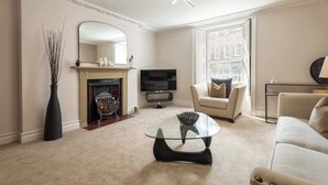 A living room with a fireplace, a television, a glass coffee table, and a sofa. - Host & Stay | Yule House (Alnwick)