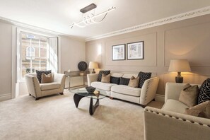 A living room with a beige sofa, two armchairs, a glass coffee table, and a modern ceiling light fixture. - Host & Stay | Yule House (Alnwick)