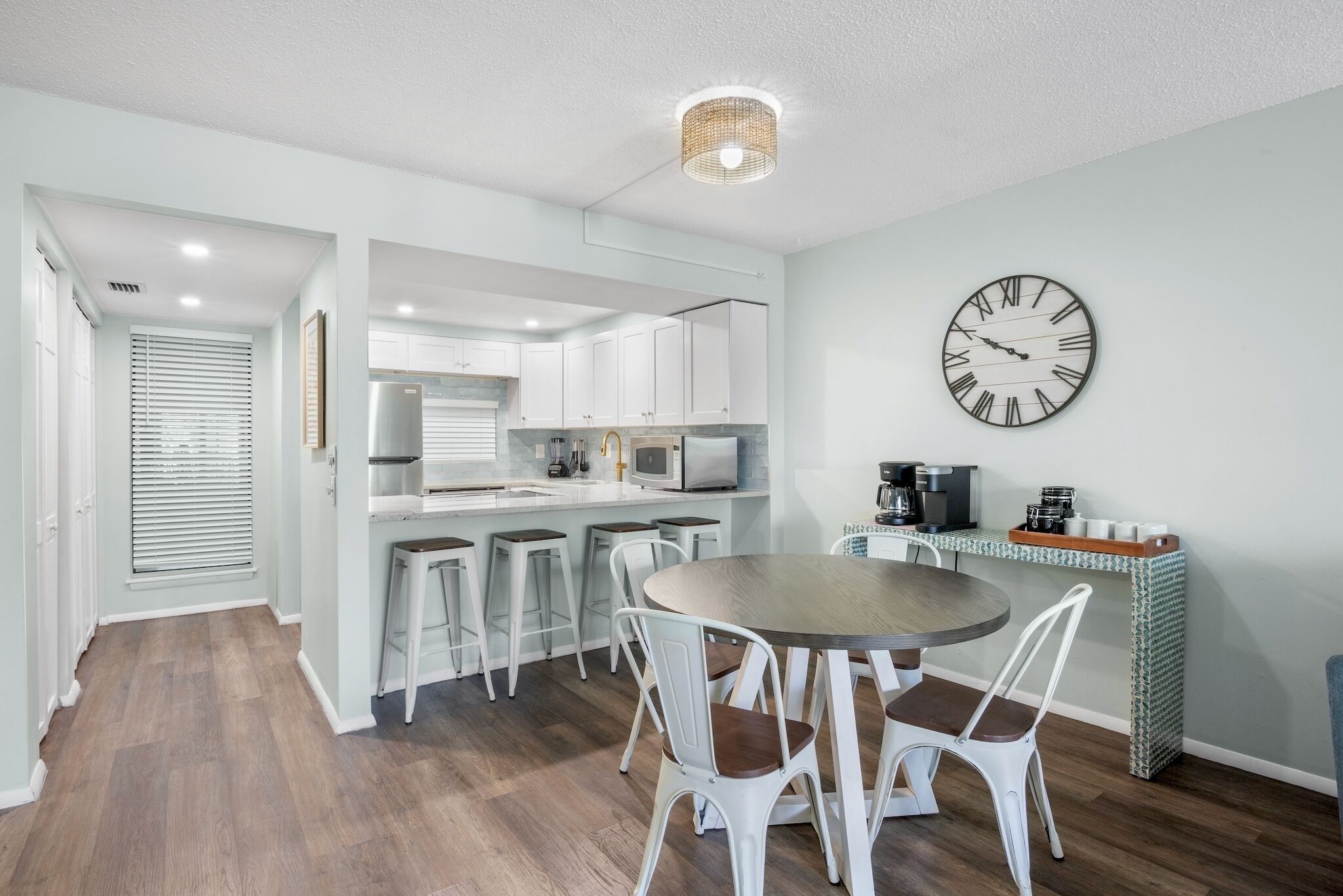 A modern kitchen with white cabinets, a round dining table with white chairs, and a wall clock.