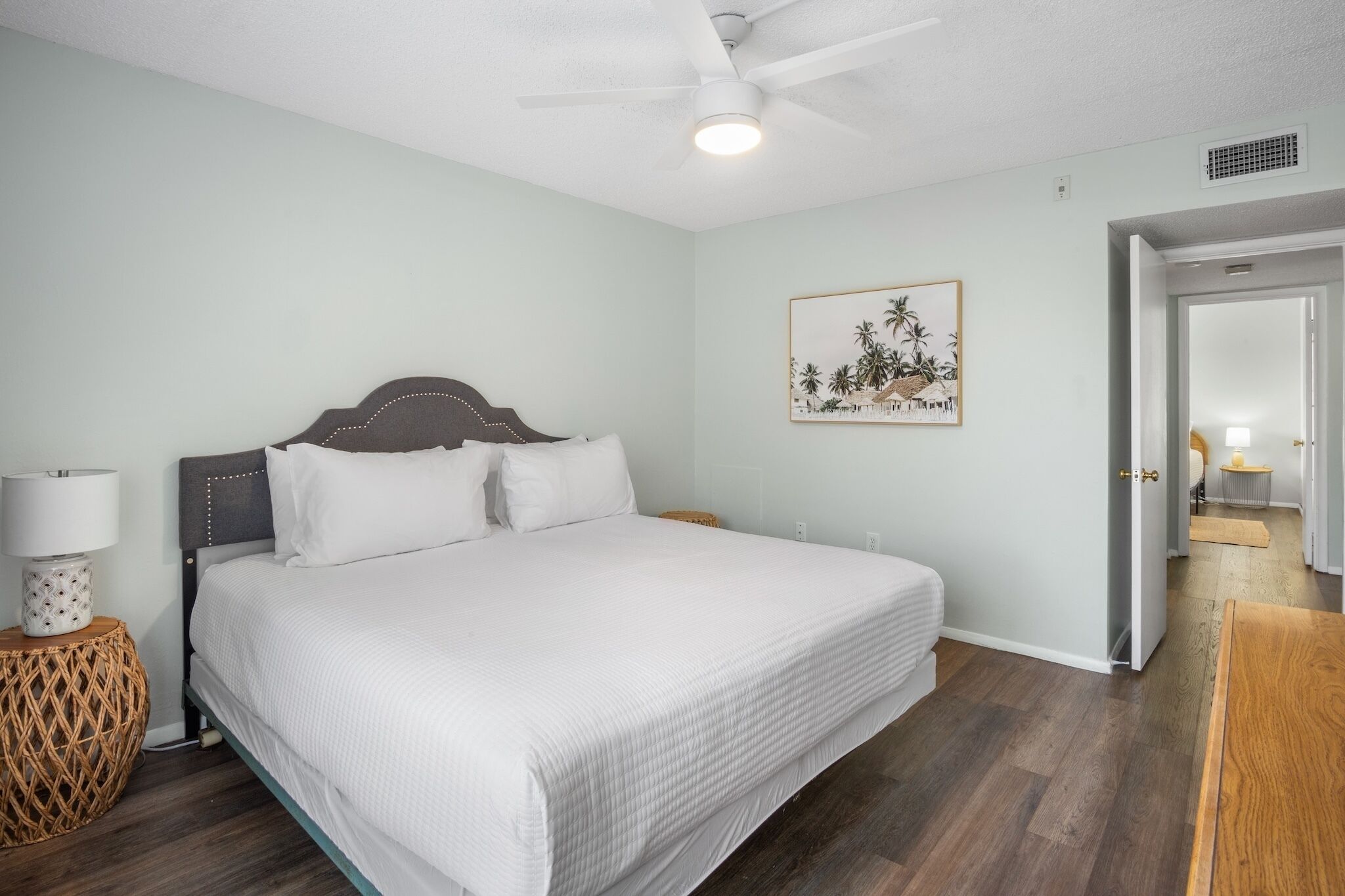 Quarto com cama, luminária de cabeceira, quadro na parede e porta para outro cômodo.
