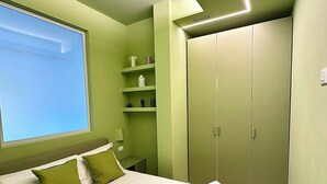 A bedroom with a bed, green walls, a window, a wardrobe, and a shelf with toiletries. - Delightful apartment with modern and comfortable style near the beach (Marina di Andora)