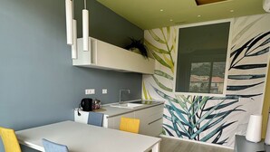 A modern kitchen with a white countertop, a sink, and a window. There is a dining table with chairs and a yellow plant on the wall. - Delightful apartment with modern and comfortable style near the beach (Marina di Andora)