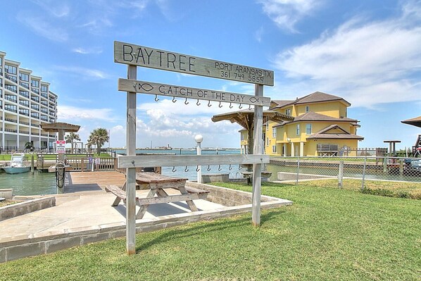 A wooden sign with 'Bay Tree' and 'Port Aransas, TX' text, a dock, a yellow building, and a marina. - Efficient studio setup with stylish accents and a comfortable atmosphere offerin (Port Aransas)