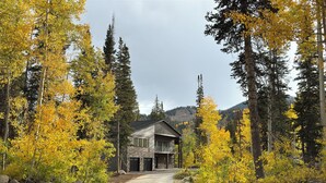Un chalet à deux étages, doté d’une façade en pierre et d’un balcon, entouré d’une forêt aux feuillages jaunes.