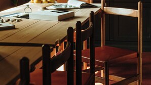A wooden dining table with chairs, a bowl of lemons, and a book.