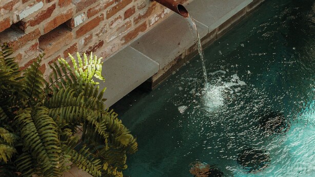A brick wall with a water feature, including a pipe and a pool.