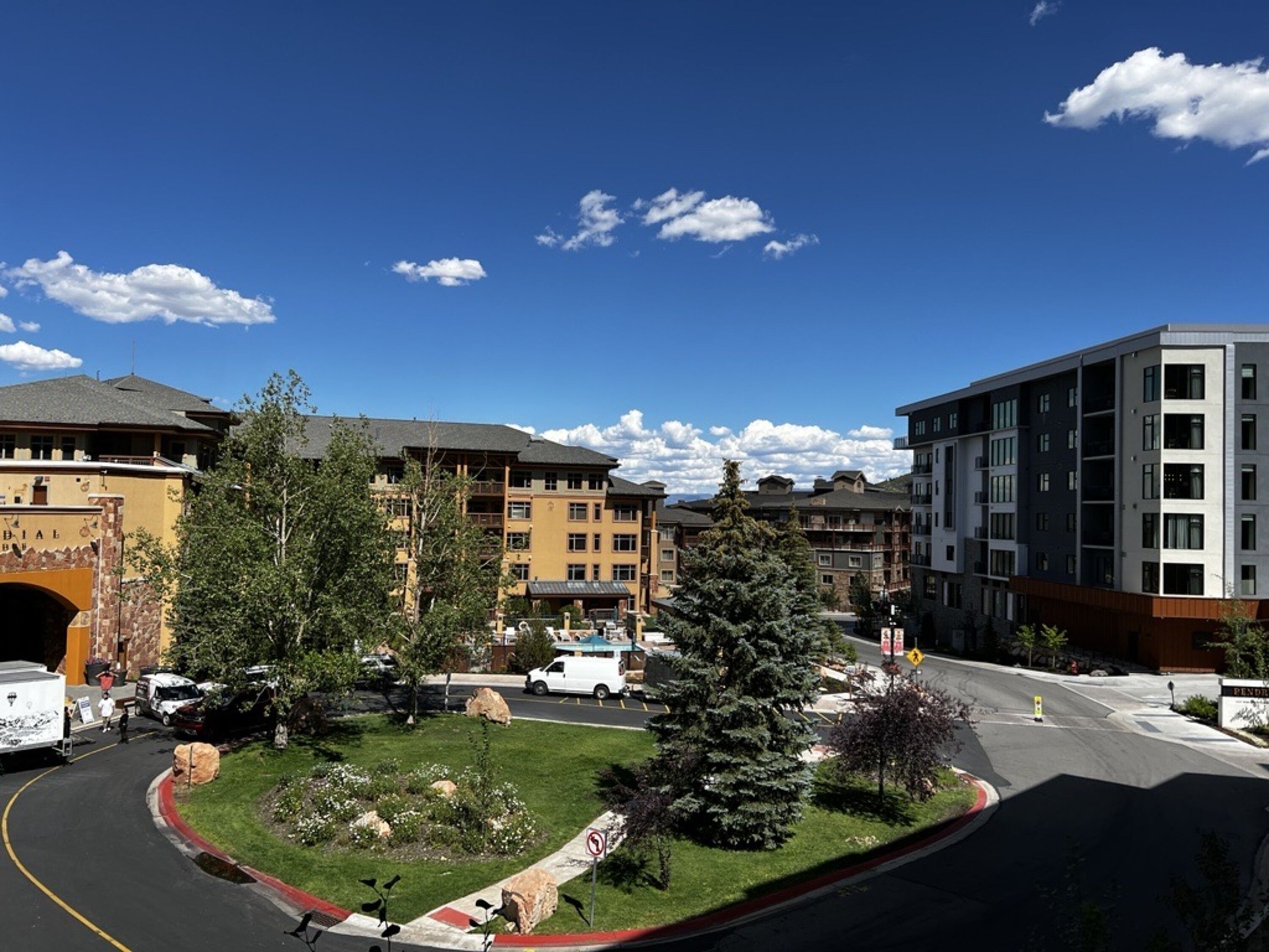 A modern building with multiple floors, a parking area, and a landscaped courtyard with trees and a small pond.