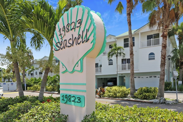 A building with a sign that reads "19823 Seashell" and a white exterior. - 🐬On Waterway🌞Sea Shell 28🏖️Quick Walk to Beach🐠Fishing Dock👙Pool (Indian Shores)