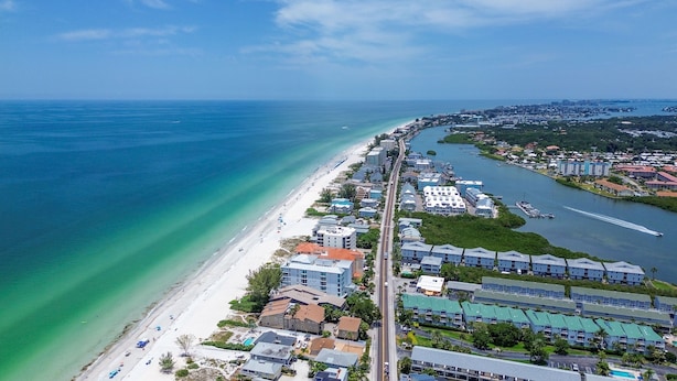 An aerial view of a coastal area with a beach, a marina, and a row of hotels along the waterfront.