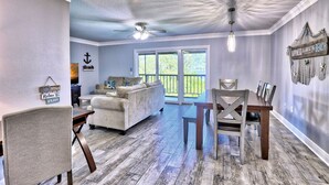 A spacious living room with a large window, a ceiling fan, and a dining area with a wooden table and chairs.