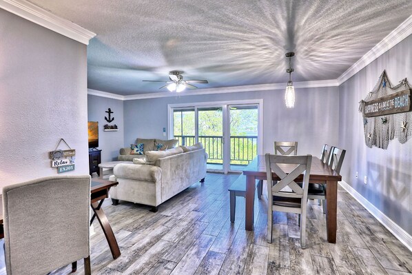 A spacious living room with a large window, a ceiling fan, and a dining area with a wooden table and chairs.