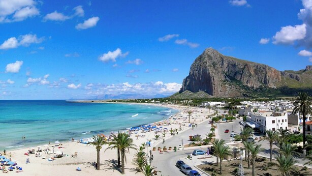 Un pueblo costero con playa, una montaña imponente y una mezcla de edificios residenciales y comerciales.