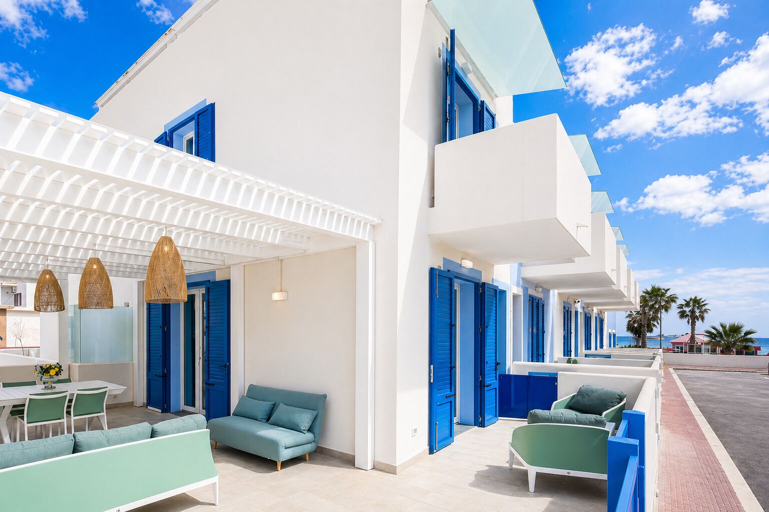 A modern hotel with a covered outdoor seating area, a pool, and a view of the sea.