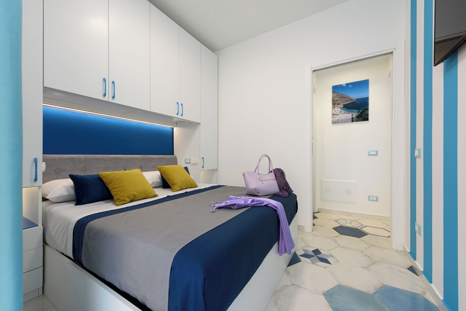 Un dormitori modern amb un llit, un capçal, una tauleta de nit i una porta que dona a una altra habitació.