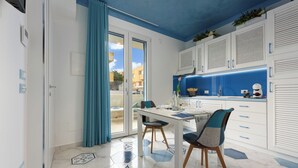 Una cocina moderna con salpicadero azul, armarios blancos y un comedor con mesa y sillas de vidrio.