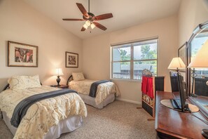 A bedroom with two beds, a ceiling fan, a desk with a computer, and a window with a view of a fence and trees. - Lakefront Lodge by Innsbrook Vacations! (Innsbrook)