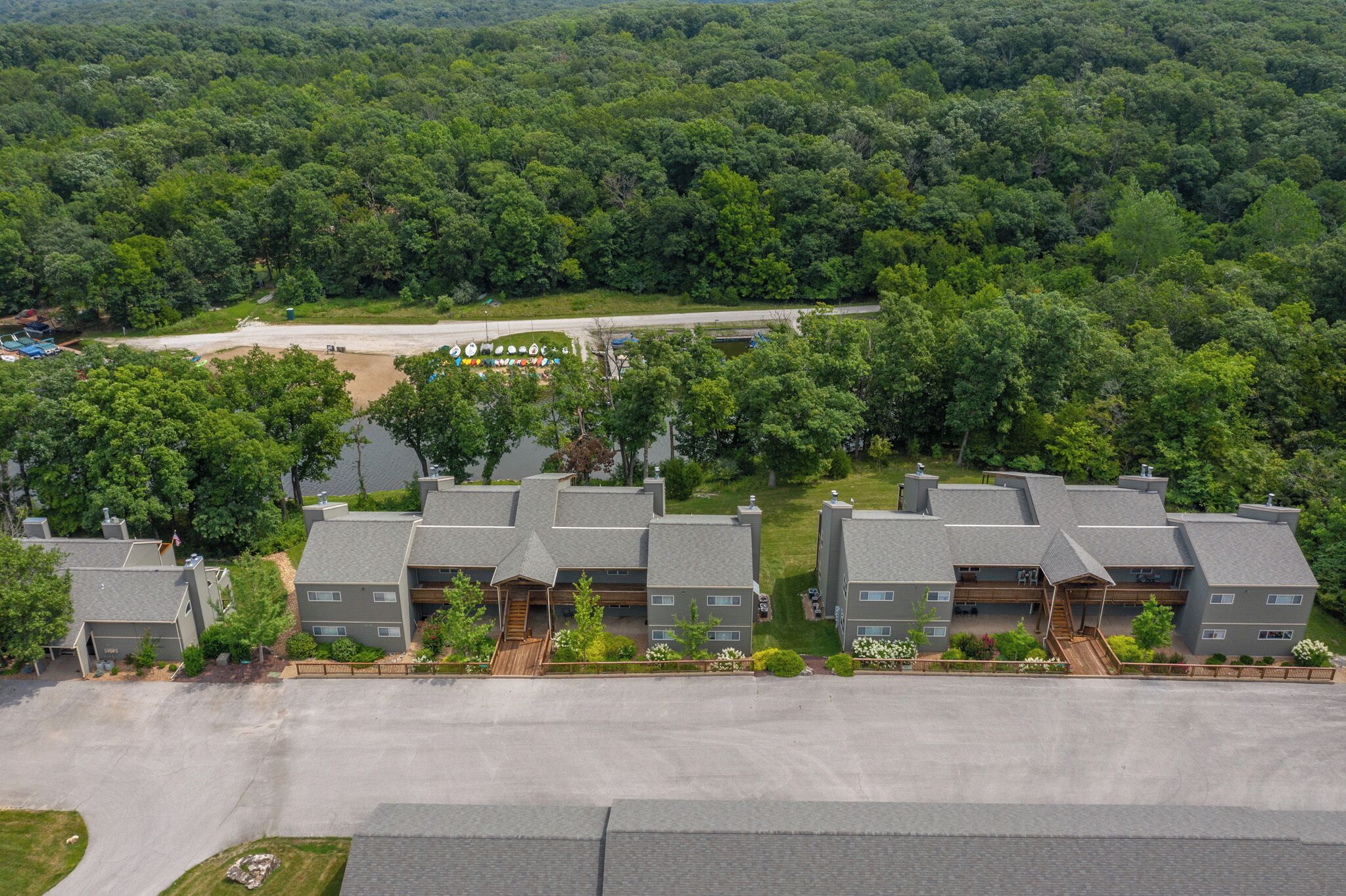 Un quartier résidentiel composé de nombreuses maisons à deux étages, une rue principale et une forêt dense en arrière-plan.