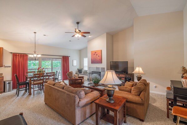 A spacious living room with a fireplace, a television, and a dining area with a red curtain. - Lakefront Lodge by Innsbrook Vacations! (Innsbrook)