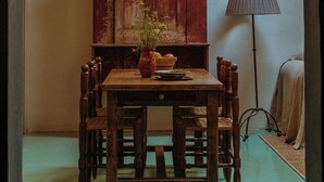 A dining area with a wooden table and chairs, a vase with a plant, a red cabinet, and a floor lamp. - Designer Bywater Carriage House w/ Pool & Courtyard Near Frenchmen (New Orleans)