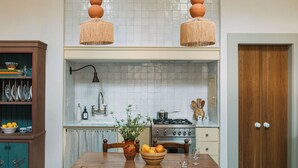 A kitchen with a wooden table, a stove, and a hanging light fixture. - Designer Bywater Carriage House w/ Pool & Courtyard Near Frenchmen (New Orleans)