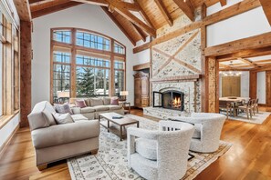 A spacious living room with a fireplace, large windows, and wooden beams. - Luxe Retreat by InvitedHome | Private Ski-In/Out Cabin, Hot Tub, Pool Table (Edwards)