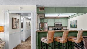 Una cocina con gabinetes verdes, un refrigerador de acero inoxidable y una zona de bar con sillas de mimbre.