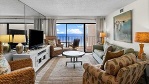 Un salón espacioso con un televisor de pantalla plana grande, muebles de mimbre, una mesa de centro redonda y un balcón con vista al mar.