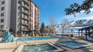 A swimming pool area with a hot tub, lounge chairs, and a view of a mountain.