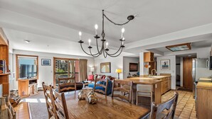 A spacious living room with a wooden dining table, a chandelier, and a television.