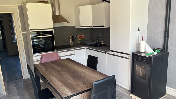 A compact kitchen with a wooden table and chairs, a built-in oven, and a black refrigerator.