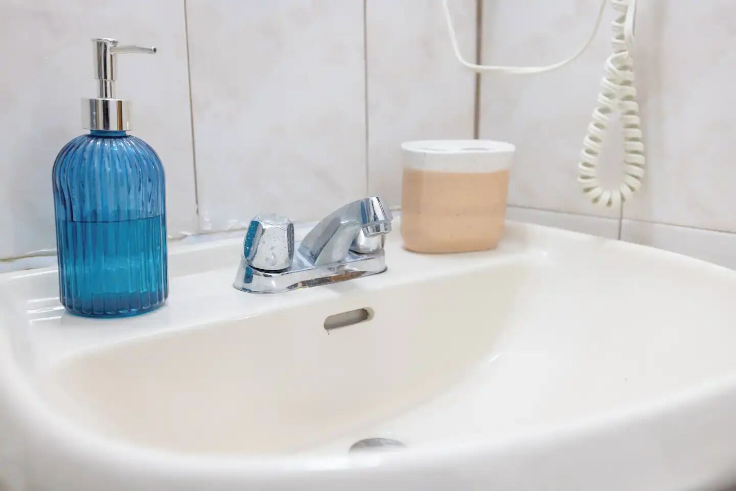 Un lavabo de salle de bain avec un distributeur de savon bleu, un robinet et un savon en barre.