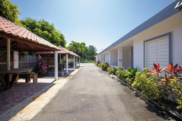 A corridor with a covered seating area on the left and a row of rooms on the right, separated by a pathway.