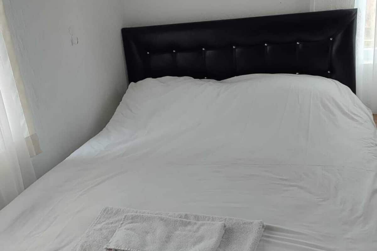 A neatly made bed with a white mattress and a grey blanket folded on top.
