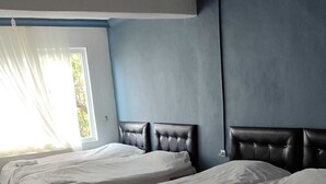 Ein Hotelzimmer mit vier nebeneinander liegenden Betten, einem großen Fenster mit Vorhängen und einer blauen Wand.